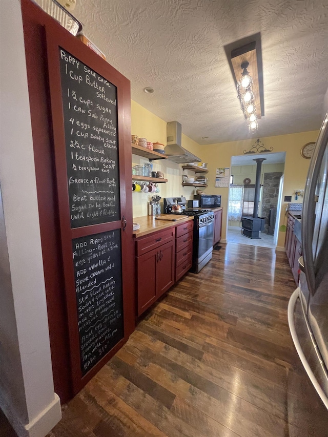 kitchen featuring a wood stove, dark wood finished floors, wall chimney exhaust hood, and gas range oven