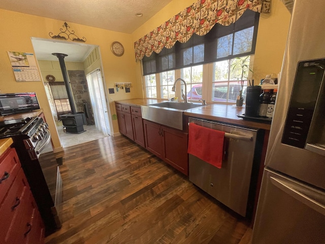 kitchen featuring dark wood finished floors, a wood stove, a sink, appliances with stainless steel finishes, and a textured ceiling