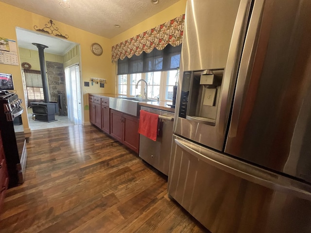 kitchen with a sink, a textured ceiling, dark wood finished floors, appliances with stainless steel finishes, and a wood stove