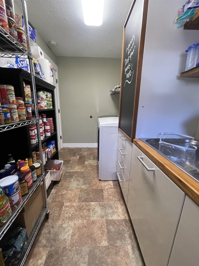 washroom with stone finish floor, a textured ceiling, baseboards, washer / dryer, and laundry area