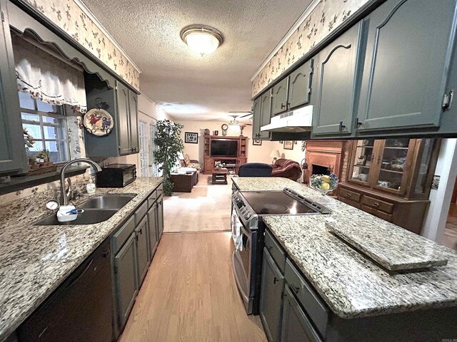 kitchen featuring light wood finished floors, under cabinet range hood, stainless steel range with electric stovetop, a textured ceiling, and a sink