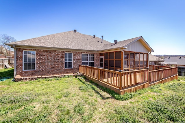 rear view of property featuring fence, a yard, roof with shingles, a sunroom, and brick siding