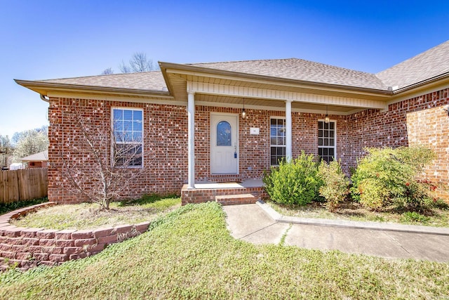 property entrance featuring fence, brick siding, covered porch, and a shingled roof