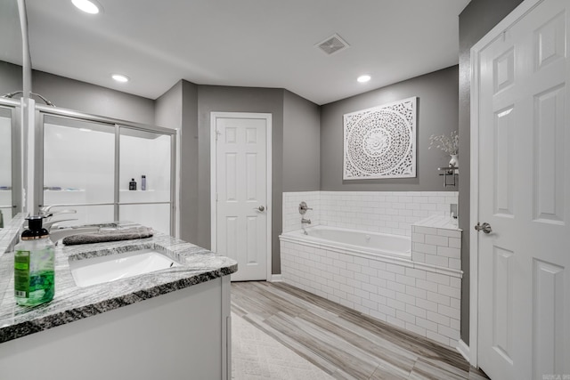 bathroom with wood finished floors, visible vents, double vanity, a stall shower, and a garden tub