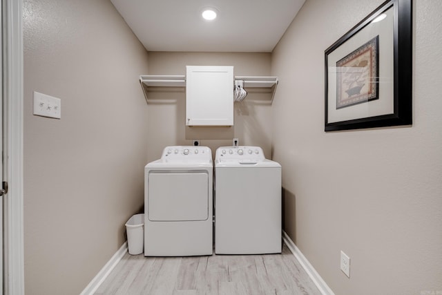 clothes washing area with baseboards, cabinet space, light wood-type flooring, and washer and clothes dryer