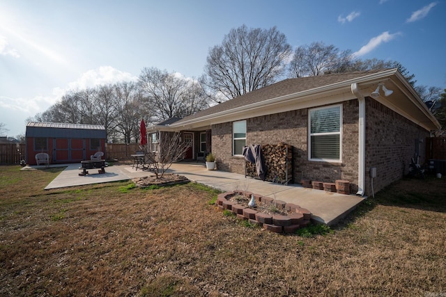 rear view of house featuring a lawn, fence, an outdoor fire pit, an outdoor structure, and a patio area