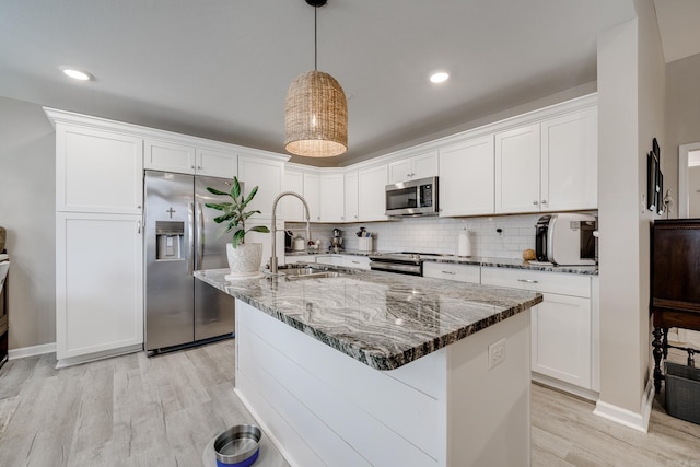 kitchen featuring dark stone countertops, a sink, decorative backsplash, appliances with stainless steel finishes, and white cabinetry