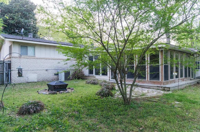 back of house with brick siding, a fire pit, a yard, and a sunroom