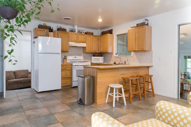 kitchen with visible vents, under cabinet range hood, backsplash, white appliances, and a peninsula