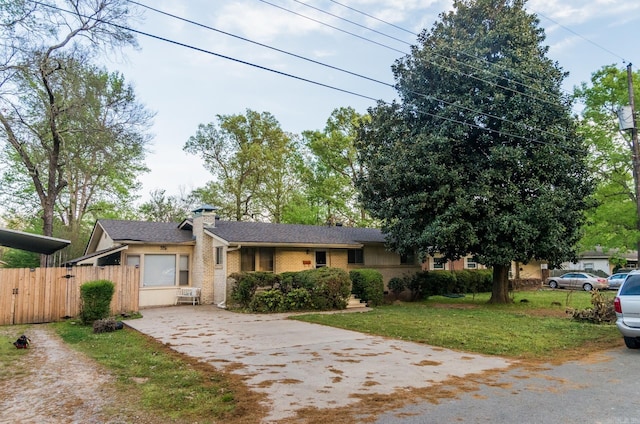 view of front of house featuring fence, driveway, a chimney, a front lawn, and brick siding