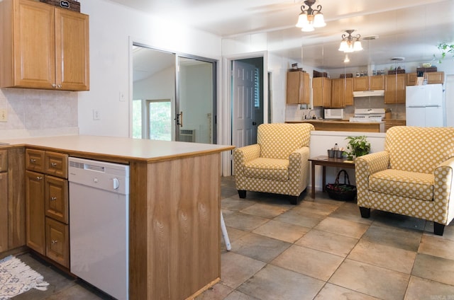 kitchen with backsplash, under cabinet range hood, light countertops, a peninsula, and white appliances