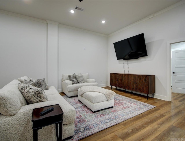 living room with visible vents, wood finished floors, baseboards, and ornamental molding