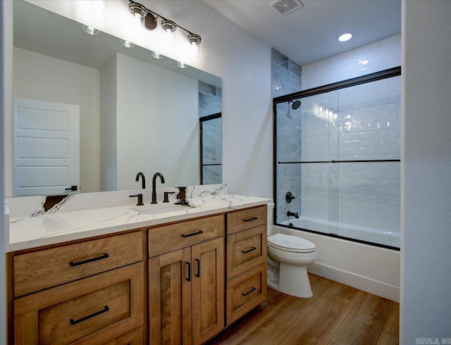 full bathroom with visible vents, bath / shower combo with glass door, toilet, wood finished floors, and vanity