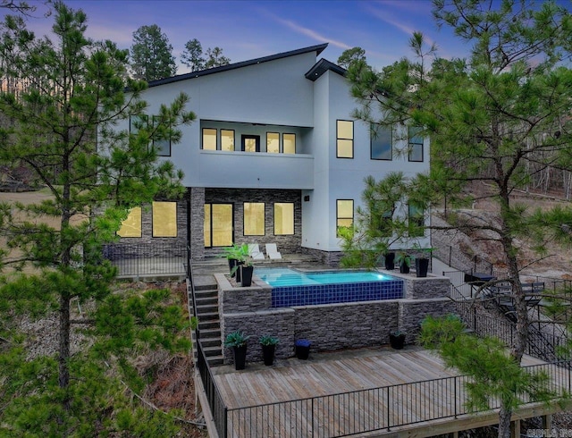 back of house at dusk featuring a patio, an outdoor pool, stone siding, and stucco siding