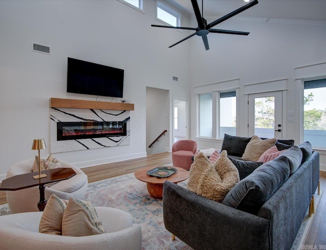 living area featuring visible vents, a glass covered fireplace, wood finished floors, a high ceiling, and ceiling fan