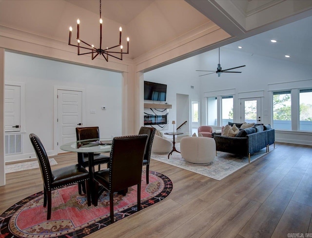 dining room with beam ceiling, high vaulted ceiling, wood finished floors, and ceiling fan with notable chandelier