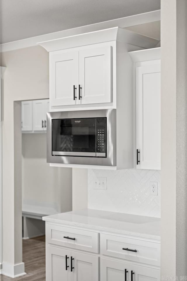 details featuring white cabinetry, tasteful backsplash, wood finished floors, and built in microwave