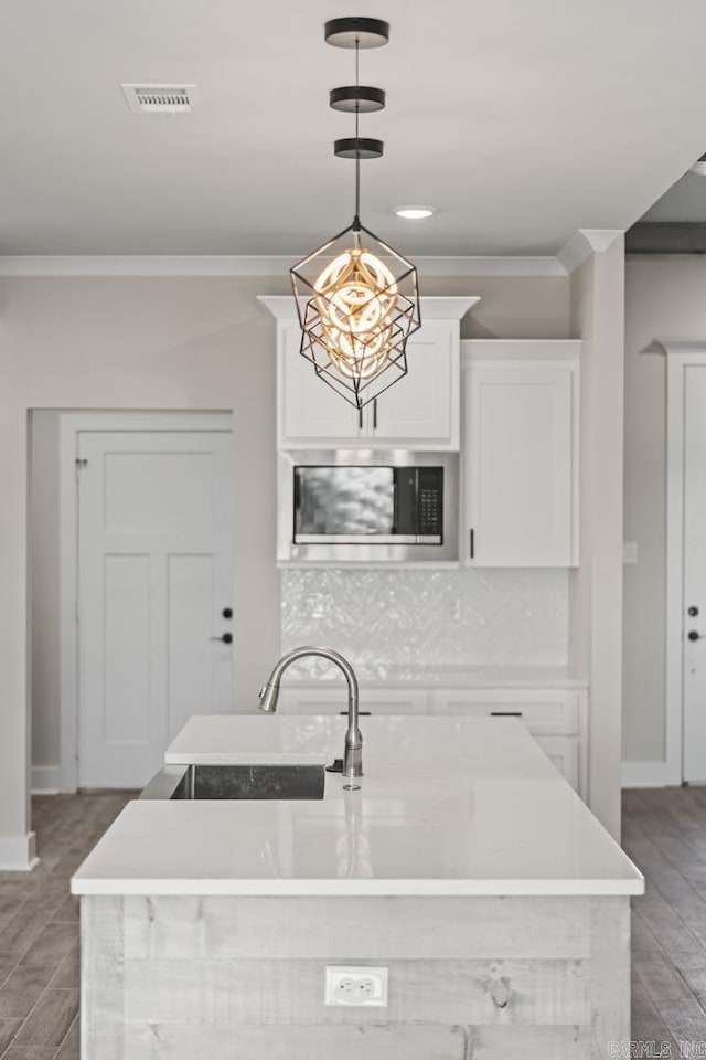 kitchen with visible vents, backsplash, stainless steel microwave, crown molding, and white cabinetry