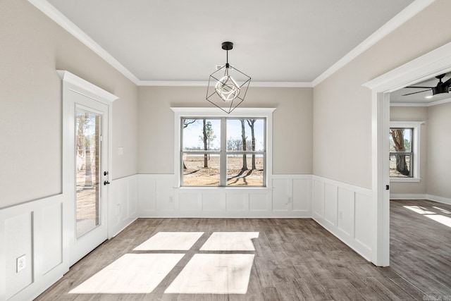 unfurnished dining area with wainscoting, wood finished floors, ornamental molding, and ceiling fan with notable chandelier