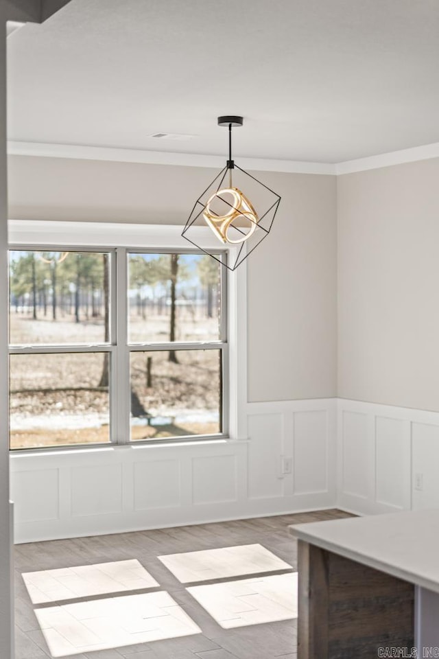 unfurnished dining area with a chandelier, a decorative wall, light wood-type flooring, and crown molding