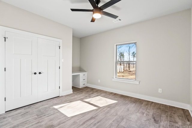 unfurnished bedroom featuring light wood-type flooring, visible vents, a ceiling fan, a closet, and baseboards