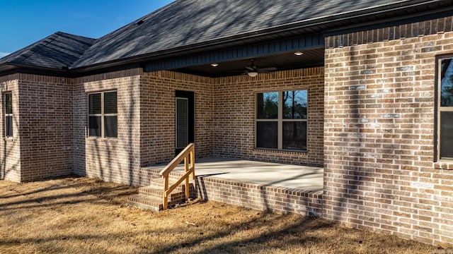 property entrance with brick siding, a patio, ceiling fan, and roof with shingles