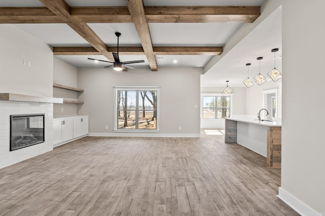 unfurnished living room with baseboards, ceiling fan, a tiled fireplace, light wood-type flooring, and beam ceiling