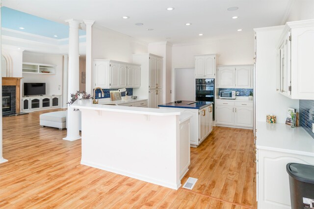 kitchen with a peninsula, black appliances, white cabinets, light wood-style floors, and a kitchen bar