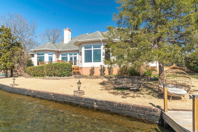 back of property with a deck with water view, a chimney, and stucco siding