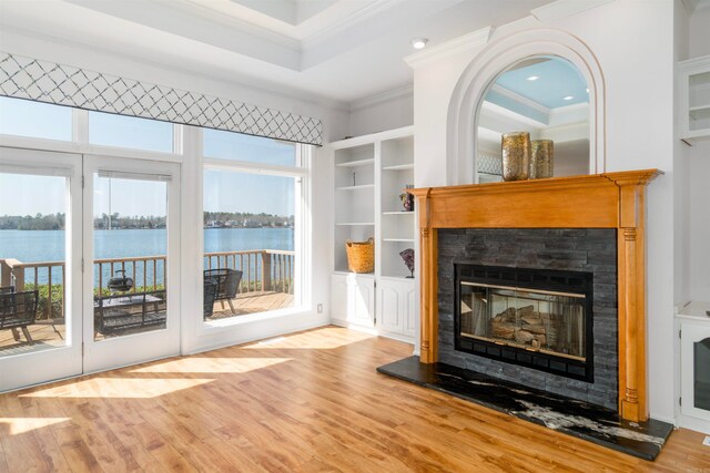 unfurnished living room featuring a water view, ornamental molding, built in features, wood finished floors, and a glass covered fireplace