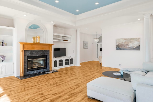 living area featuring built in shelves, wood finished floors, recessed lighting, a glass covered fireplace, and crown molding