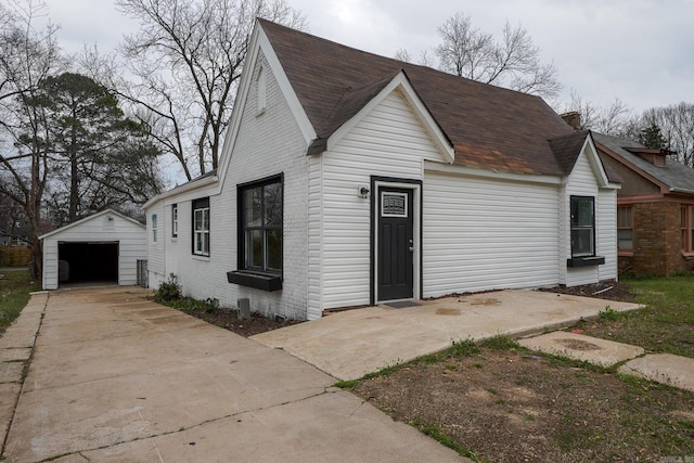 view of front of house with brick siding, a detached garage, roof with shingles, an outdoor structure, and driveway