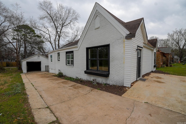 view of home's exterior featuring a detached garage, brick siding, an outdoor structure, and driveway