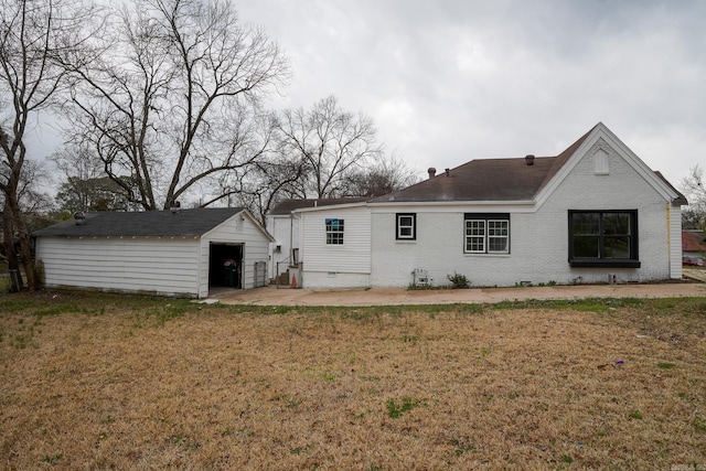 back of property with an outbuilding, a patio area, a lawn, and brick siding