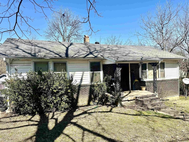 view of front of house featuring a front yard, brick siding, roof with shingles, and a chimney