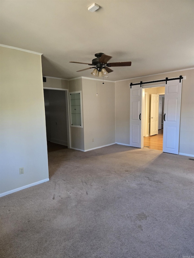 spare room featuring a barn door, carpet flooring, ceiling fan, and ornamental molding