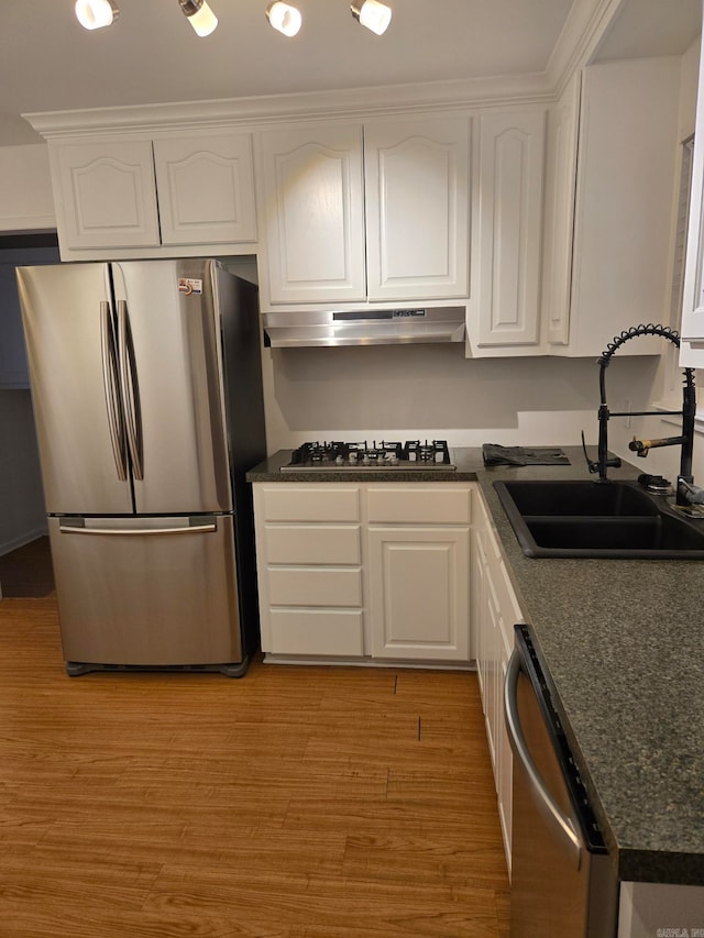 kitchen with a sink, stainless steel appliances, under cabinet range hood, and white cabinetry