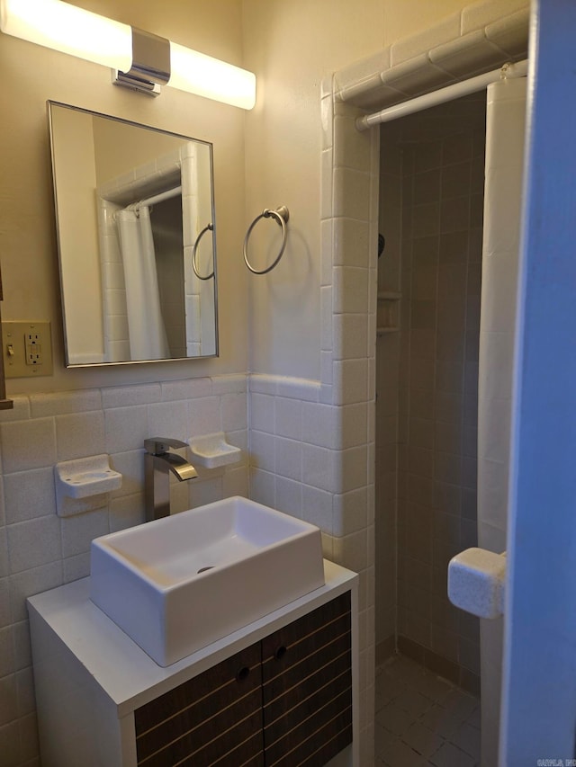 bathroom with a wainscoted wall, tile walls, vanity, and a tile shower