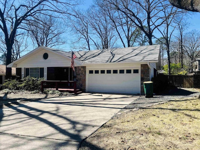 ranch-style house with stone siding, an attached garage, concrete driveway, and fence