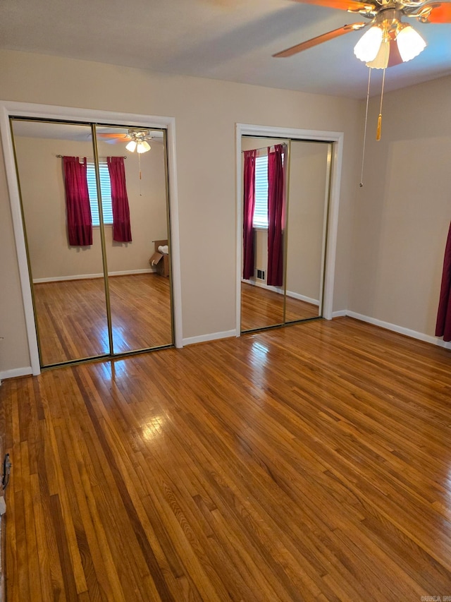 unfurnished bedroom featuring multiple windows, wood finished floors, and two closets