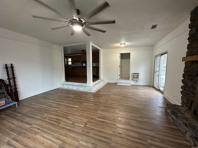 unfurnished living room with visible vents, heating unit, wood finished floors, and a ceiling fan