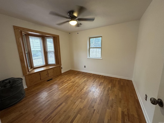 unfurnished room featuring a ceiling fan, wood finished floors, visible vents, and baseboards