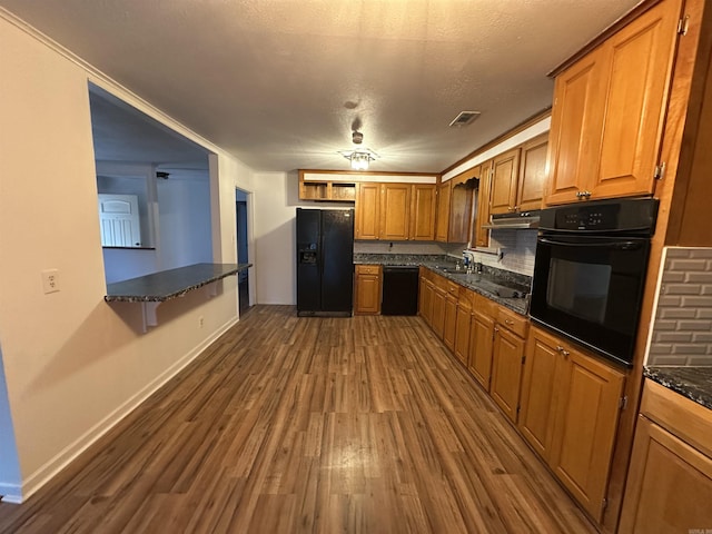 kitchen featuring dark wood-style floors, brown cabinetry, visible vents, a sink, and black appliances