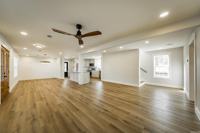 unfurnished living room featuring visible vents, stairway, light wood-type flooring, and ceiling fan