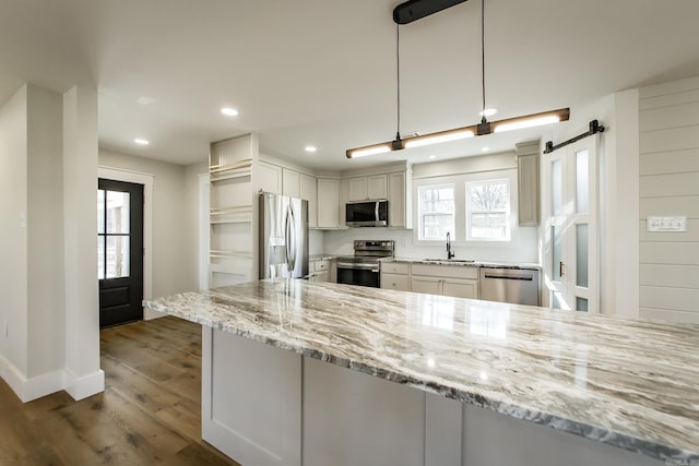 kitchen with a sink, stainless steel appliances, light stone counters, and dark wood finished floors