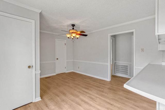 empty room with a textured ceiling, ceiling fan, ornamental molding, and light wood finished floors