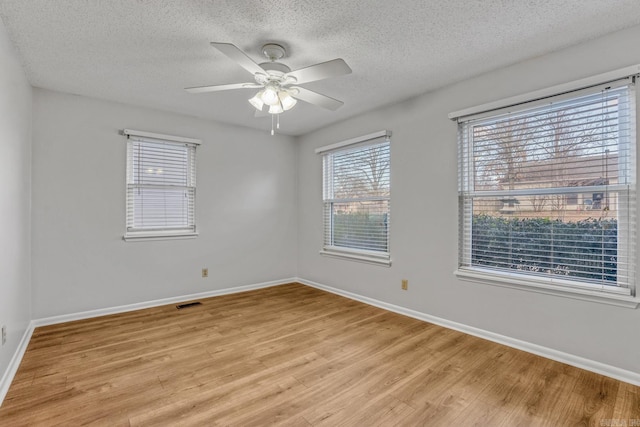 unfurnished room with a ceiling fan, visible vents, baseboards, light wood finished floors, and a textured ceiling