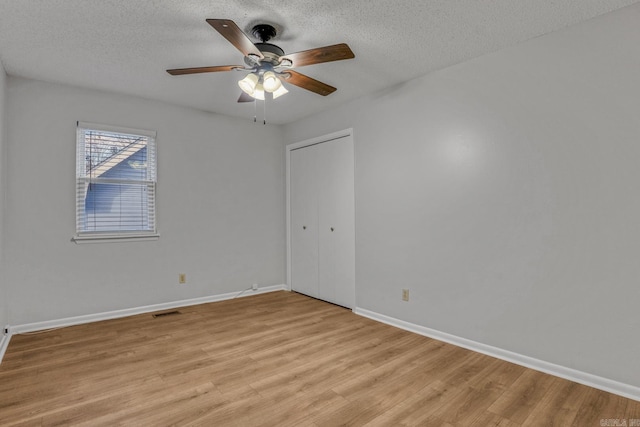 empty room featuring visible vents, light wood-style flooring, a textured ceiling, and a ceiling fan