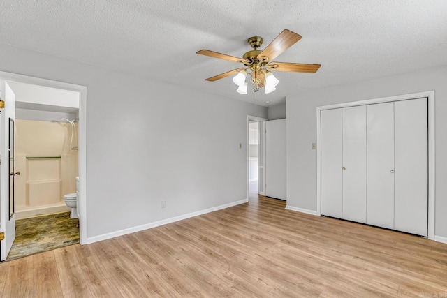 unfurnished bedroom featuring baseboards, light wood-type flooring, ensuite bathroom, a closet, and a textured ceiling