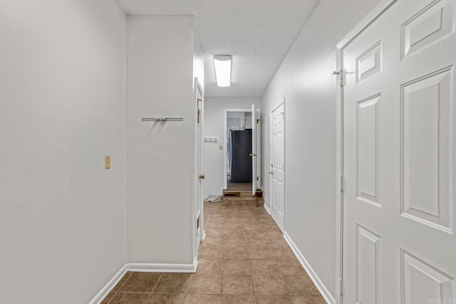 corridor with tile patterned floors, baseboards, and a textured ceiling